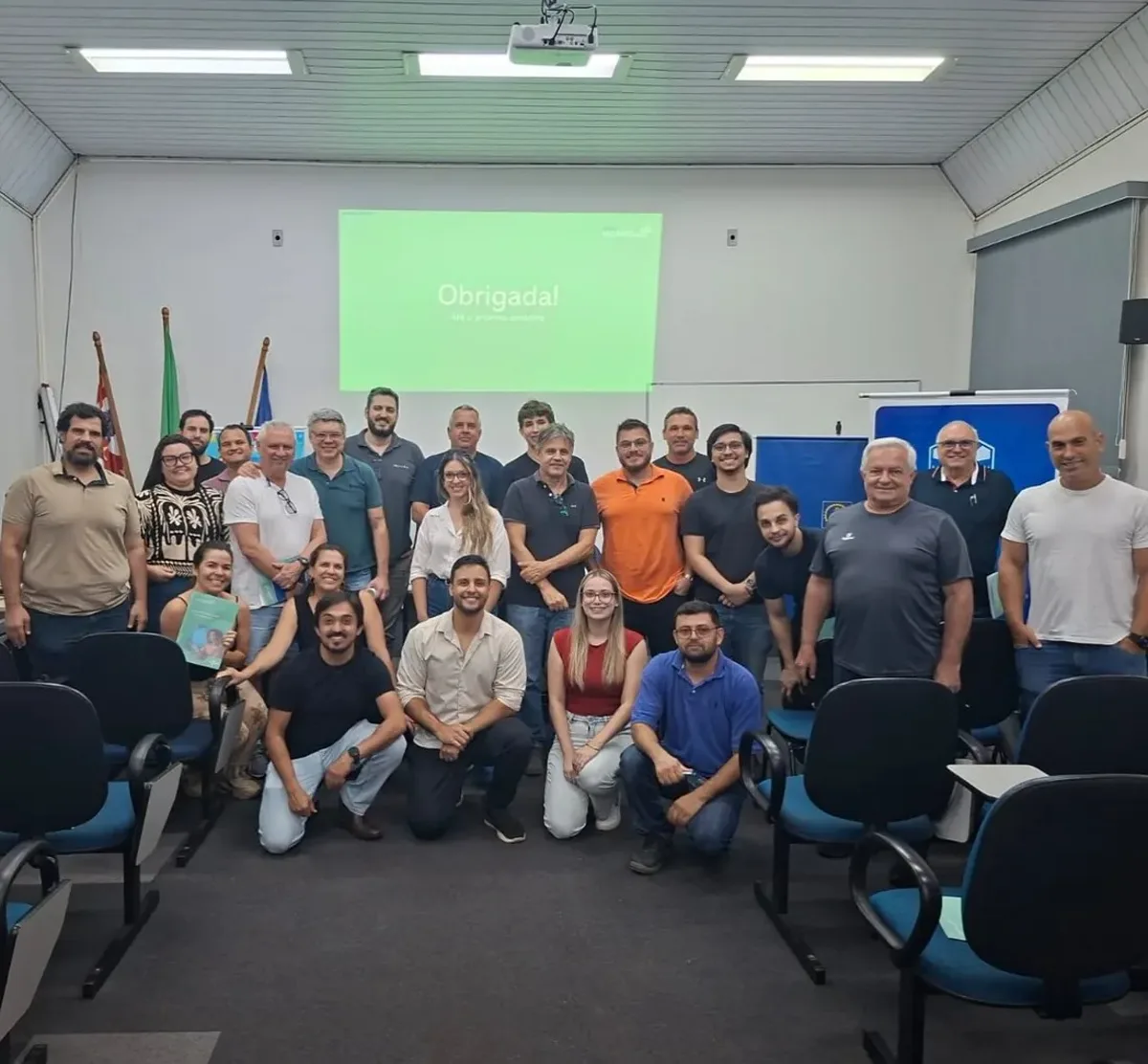 Turma de IA da Alpha Fox em São Carlos reunida em auditório, com cerca de trinta participantes posando em frente à tela de projeção